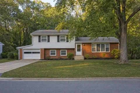Brick and siding split-level house with a lower-level garage and mulched beds in front of mature trees in Beltsville, Maryland