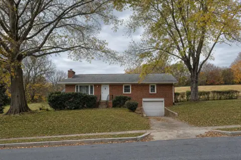 Brick rambler with a lower-level garage backing onto an open field and hedgerow in Beltsville, Maryland in late fall