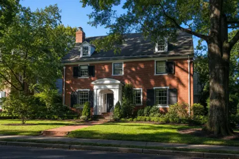 Red brick colonial home on a tree-lined residential street in Bethesda Maryland with mulch beds against the foundation