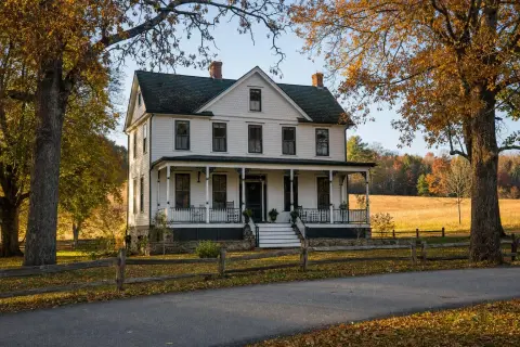 Restored 19th-century white frame farmhouse with a deep front porch beside a hay field and autumn trees in Boyds Maryland