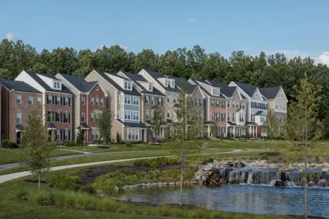 Row of newer townhomes in Brambleton Virginia beside a landscaped pond, walking trail, and wooded edge