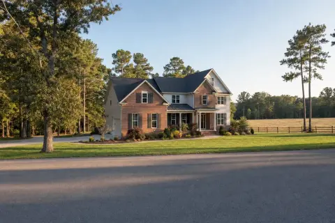 Semi-rural residential street in Brandywine, Maryland with a brick-and-siding home, mature oaks and pines, and a wooded treeline behind an open field