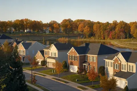 Brick-front colonial homes along a curving street above a community lake with fall trees in Bristow, Virginia