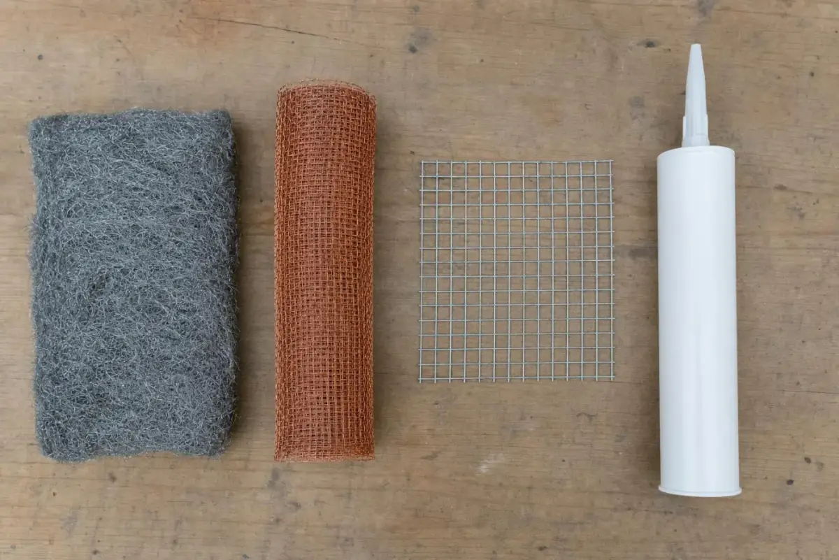 Steel wool pad, roll of copper mesh, square of quarter-inch hardware cloth and a tube of caulk laid out on a workbench