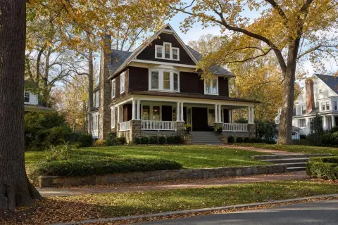 Autumn street in Chevy Chase Village, Maryland with an early-1900s shingle-style house, a wide front porch, and mature oak trees