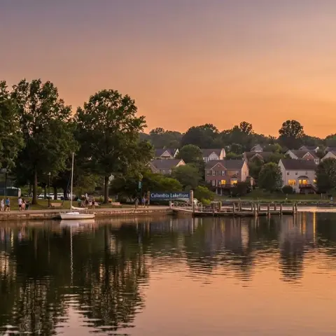 Lake Kittamaqundi in Columbia, Maryland with lakefront promenade and mature trees reflected in calm water at golden hour