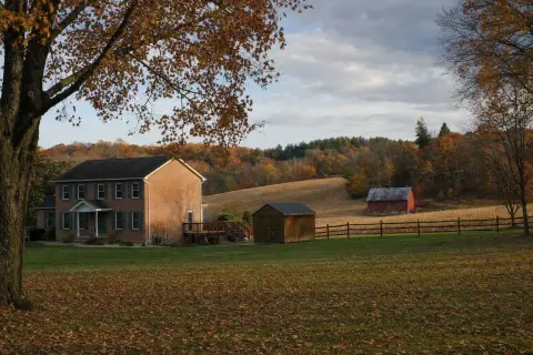 Brick colonial home with a wooden shed beside a harvested field and red barn in the rolling farmland around Damascus Maryland