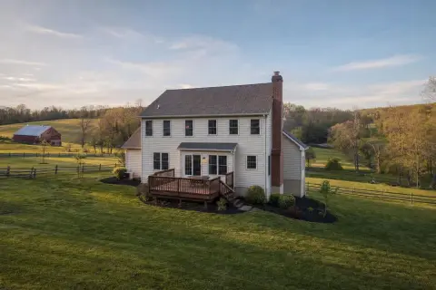 1980s two-story colonial in Damascus Maryland with a brick side chimney and back deck, with farm fields and a red barn behind it