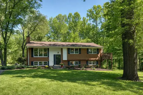 Brick split-level home in Derwood Maryland with a wooden back deck and tall oak trees from a wooded stream valley behind it
