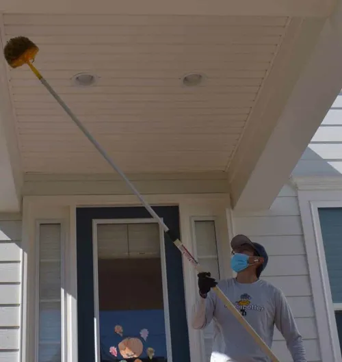 Better Termite technician removing spider webs from a porch overhang at an Ashburn Village colonial home