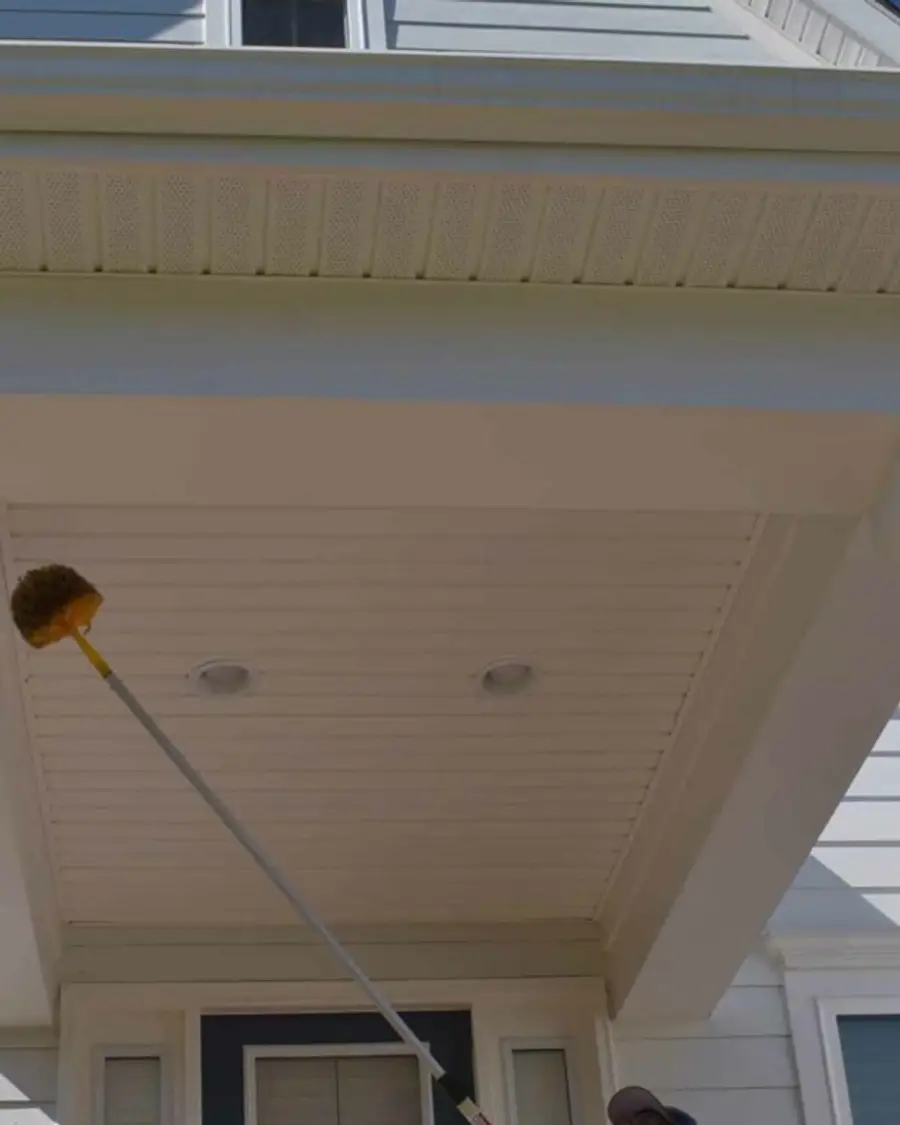 Pest control technician using webster tool to remove spider webs from porch ceiling