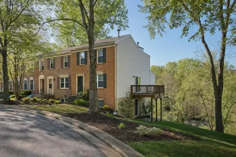 Row of brick-front townhomes in Germantown Maryland with a wooden deck over a walk-out basement above a wooded stream valley