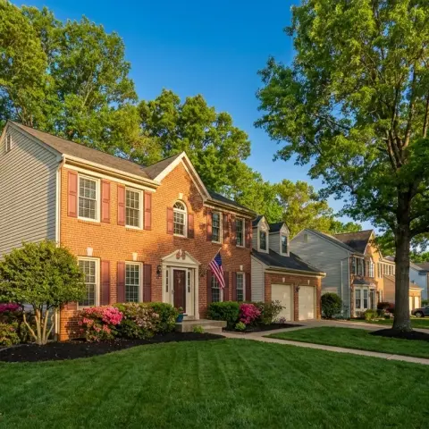 Charming suburban residential street in Herndon Virginia with colonial-style homes, mature oak trees, and mulch beds along foundations