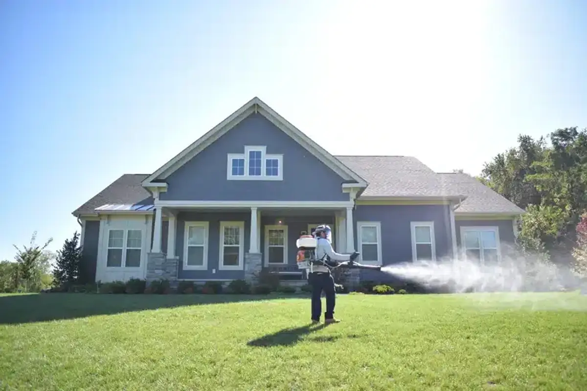 Technician applying perimeter treatment around a home exterior with sprayer