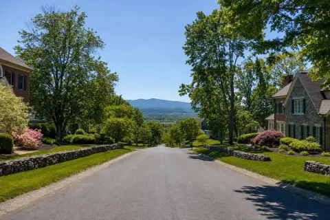 Late-spring residential street in Loudoun County Virginia with brick colonial homes, fresh mulch beds, and the Blue Ridge Mountains in the distance
