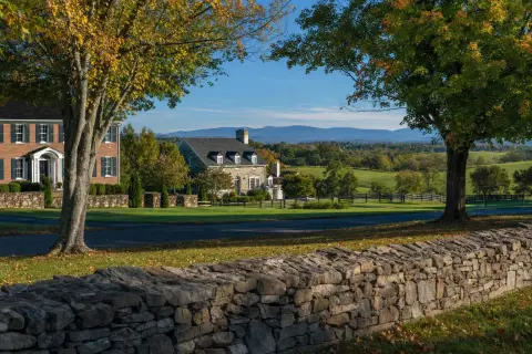 Residential street in Loudoun County Virginia with brick colonial homes, a stacked stone wall, and the Blue Ridge Mountains in the distance