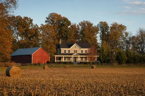 Farmhouse and red barn beside a harvested cornfield with hay bales in rural Nokesville, Virginia in autumn