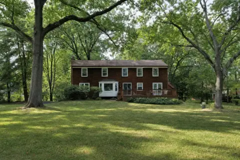 1980s wood-sided colonial home in Olney Maryland with a bay window and back deck under tall oak and tulip poplar trees