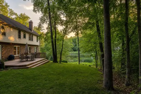 Backyard deck of a brick colonial home in Olney, Maryland, with a lawn sloping to a wooded stream buffer and a cattail-lined pond