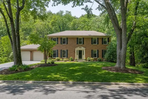 Brick-front 1970s colonial home in Olney Maryland with a concrete front stoop, mulched beds and a wooded stream valley behind it