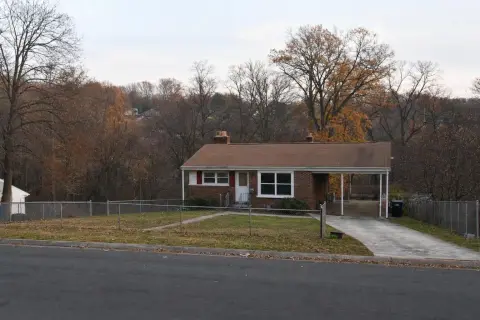Brick rambler with a carport and chain-link fence backing onto a wooded stream valley in Oxon Hill, Maryland in late fall