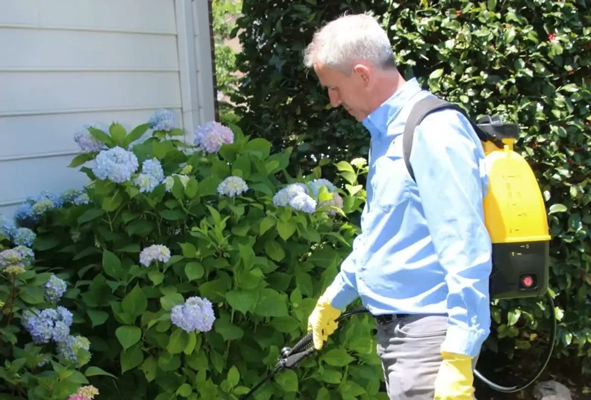 Pest control technician applying perimeter treatment along the foundation of a home