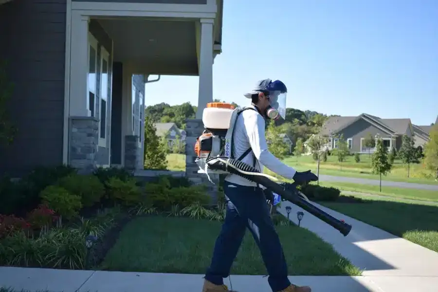 Professional pest control technician with backpack sprayer treating a home exterior