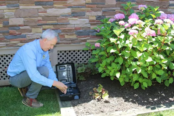 Technician servicing a rodent bait station at a Herndon Virginia home near a wooded lot