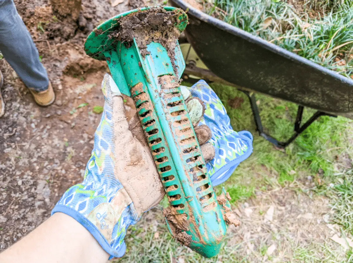 Pest control technician inspecting a termite bait station at a home foundation