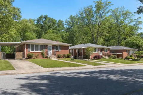 Street of 1950s red-brick rambler homes with concrete front stoops and mature trees in Temple Hills Maryland
